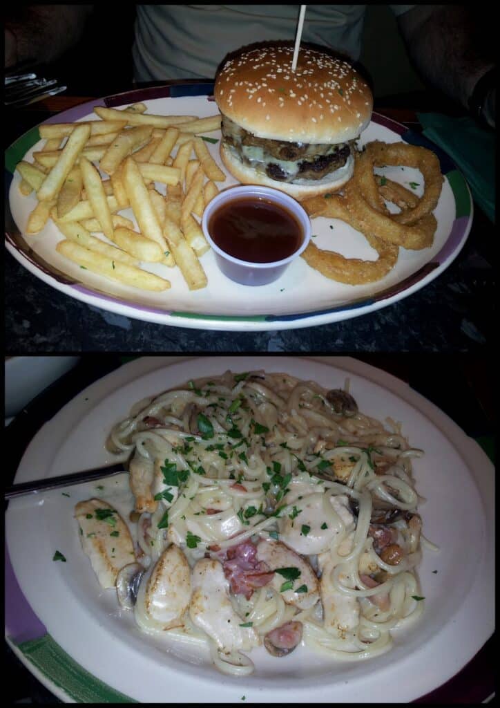 The image shows two plates of food: the top plate has a burger with a sesame seed bun, chips, onion rings, and a pot of tomato sauce; the bottom plate has creamy pasta with grilled chicken, mushrooms, bacon, and chopped parsley sprinkled on top.