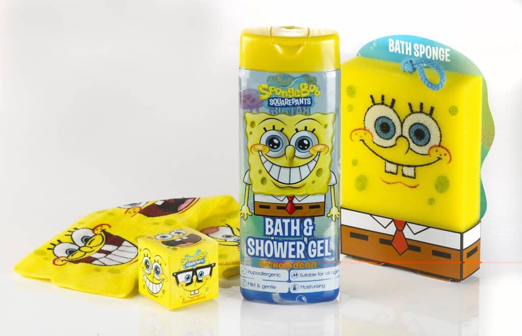 A set of SpongeBob SquarePants-themed bath products, including a yellow bath and shower gel bottle, a large bath sponge, a flannel, and a small cube sponge, all featuring cheerful images of SpongeBob’s smiling face on bright yellow backgrounds.
