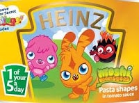 A Heinz tin label features cartoon Moshi Monsters characters: a pink creature, an orange bunny, and a small black-and-red figure. Text highlights “1 of your 5 a day” and “Pasta shapes in tomato sauce” against a yellow background.