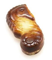 A piece of chocolate shaped like a seahorse, with a marbled pattern of milk and white chocolate, detailed with moulded features such as the fin, eye, and curled tail. The surface appears glossy and smooth.
