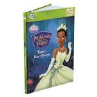 A hardback children’s book titled “The Princess and the Frog: Tiana’s New Dream” features Princess Tiana in a light green gown, tiara, and gloves, waving with a smile on a deep blue background. Disney branding is visible on the cover.