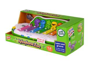 A green LeapFrog Xylophone Zoo toy box displays a colourful xylophone with five rainbow-coloured keys, each topped with an animal figure. The packaging shows musical notes and advertises learning, music, and animal sounds for ages 1–4.