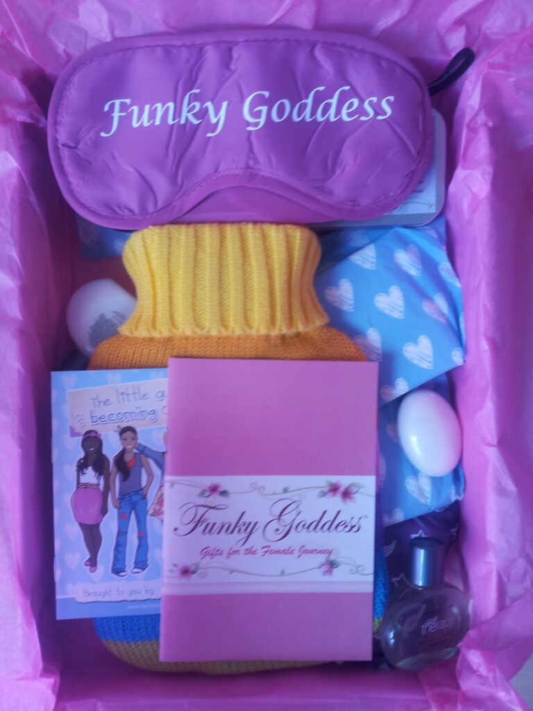 A pink box lined with tissue paper contains a purple sleep mask labelled "Funky Goddess," a yellow hot water bottle, a blue pouch with white hearts, a pink booklet titled "Funky Goddess," a small booklet, two white eggs, and a small dark bottle.