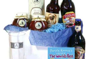 A gift set with bottled beers, jam jars, a pint glass labelled "DAD," a tin, and a card titled "The World's Best Dad," all arranged in a white box with blue tissue paper. The items are festively presented for a Father's Day celebration.