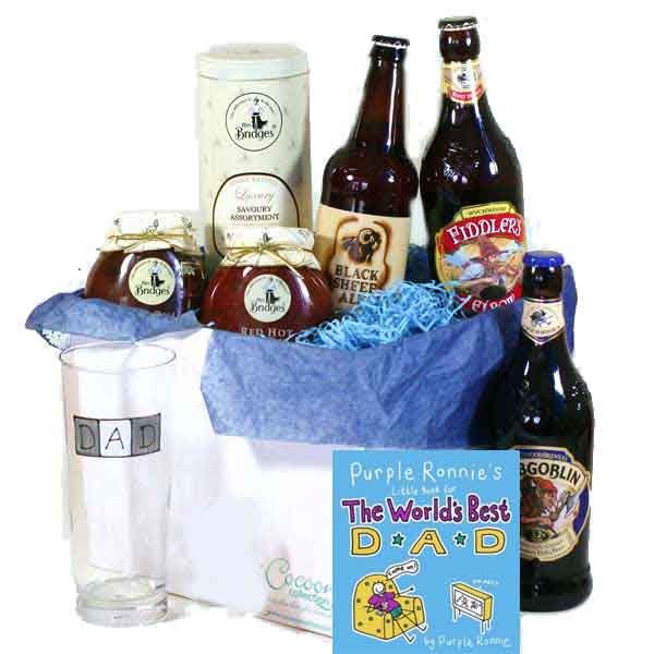 A gift set with bottled beers, jam jars, a pint glass labelled "DAD," a tin, and a card titled "The World's Best Dad," all arranged in a white box with blue tissue paper. The items are festively presented for a Father's Day celebration.