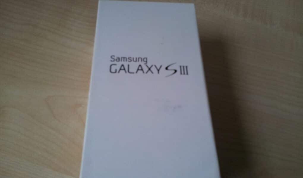 A rectangular white box with "Samsung GALAXY S III" printed in black text on the lid is placed on a light wooden surface. The box is closed and positioned slightly off-centre in the image.