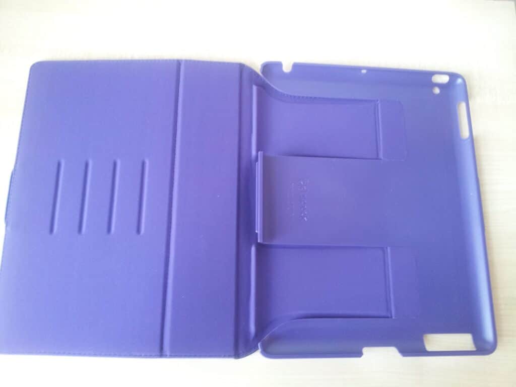 A purple plastic tablet case lies open on a white surface. The left side has three horizontal grooves, and the right side has a moulded area with cut-outs for buttons and ports. The overall material appears smooth and slightly shiny.
