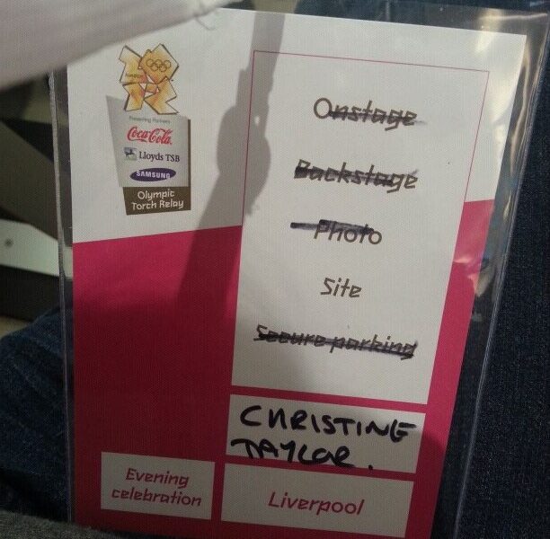 A laminated Olympic Torch Relay pass lists various access areas, with "Backstage" and "Site" checks marked and "CHRISTINE TAYLOR" hand-written. Logos for Coca-Cola, Lloyds TSB, Samsung, and Olympic Torch Relay appear. The event is in Liverpool, "Evening celebration".