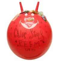 A bright red space hopper with two handles at the top, decorated with sweets and a white smiling face. Handwritten text on the front reads “Chloe Sims REEM” in black marker. The brand logo is visible above the face.