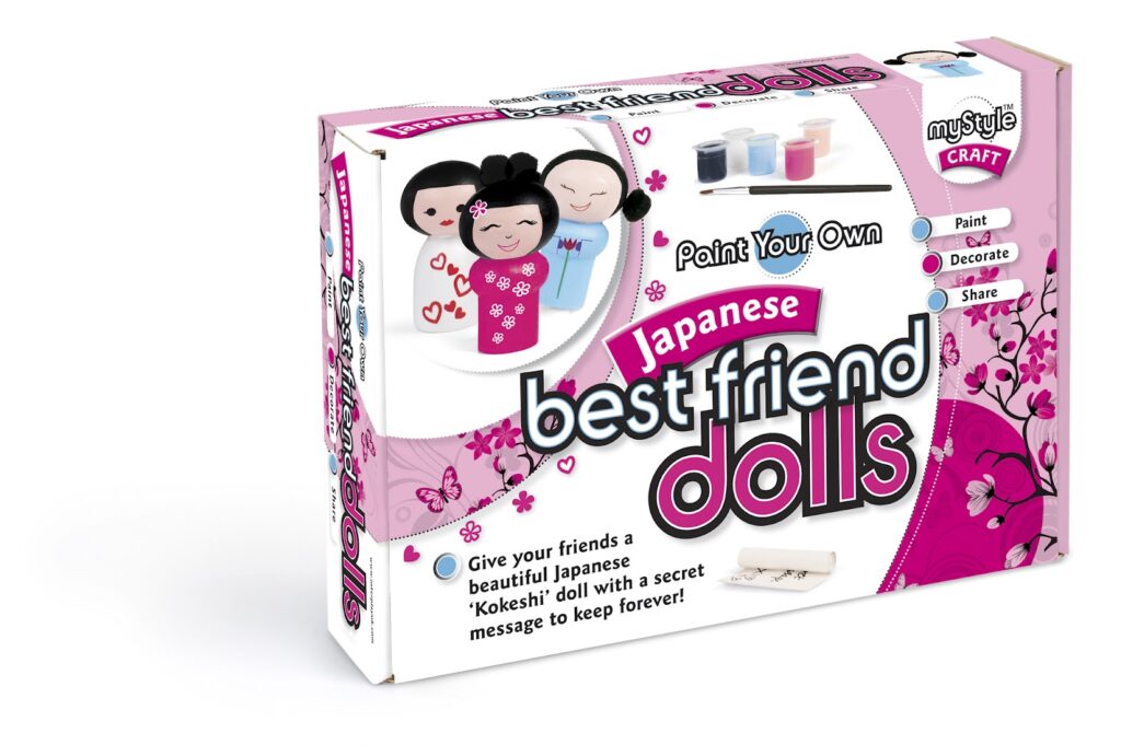 A boxed craft kit labelled "Japanese best friend dolls." The kit shows illustrations of three kokeshi-style dolls, small paint pots, a paintbrush, and cherry blossom designs. Text highlights painting, decorating, and sharing the customisable dolls.