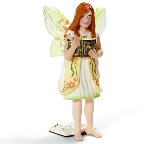 A small fairy figurine with long red hair, translucent yellow-green wings, and a cream dress adorned with orange flowers. She is barefoot and holding an open book, standing on a white base decorated with small details.