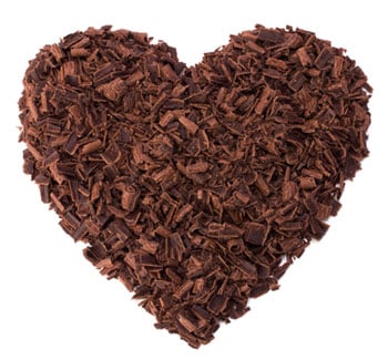 A heart shape formed from a pile of small, rough, dark chocolate shavings, arranged closely together on a white background.