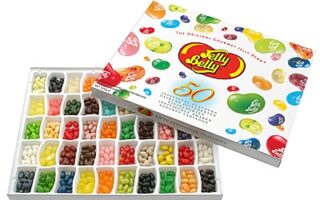 A rectangular Jelly Belly gift box, open to show 50 compartments filled with colourful assorted jelly beans. The lid, decorated with images of jelly beans and the Jelly Belly logo, rests behind the box, displaying the “50 Flavours” collection.