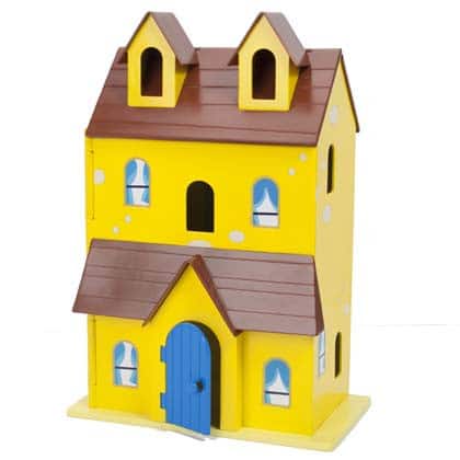 A yellow, two-storey toy house with a brown roof and two dormer windows. It has a blue arched front door, four windows with blue curtains on the ground floor, and three windows on the first floor. The house has a whimsical, cartoon-like design.