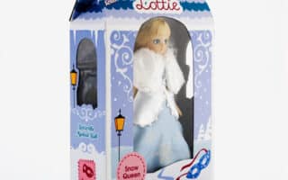 A boxed "Lottie" doll titled "Snow Queen" is shown. The doll wears a blue dress with a white fur cape. The packaging is winter-themed with snowflakes, lamp posts, and icy decorations, and features a blue handle on top.