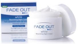 A white jar of Fade Out White Nourishing Night Cream with its lid off, showing the creamy product inside. Behind the jar, there is a blue and white product box with the same branding and text, slightly out of focus.