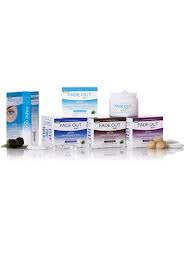 A group of Fade Out skincare products, including creams, a serum, and cleansing items, are neatly arranged in two rows on a white background. The packaging is mainly white with blue, purple, and teal accents, and some products have small natural ingredients beside them.