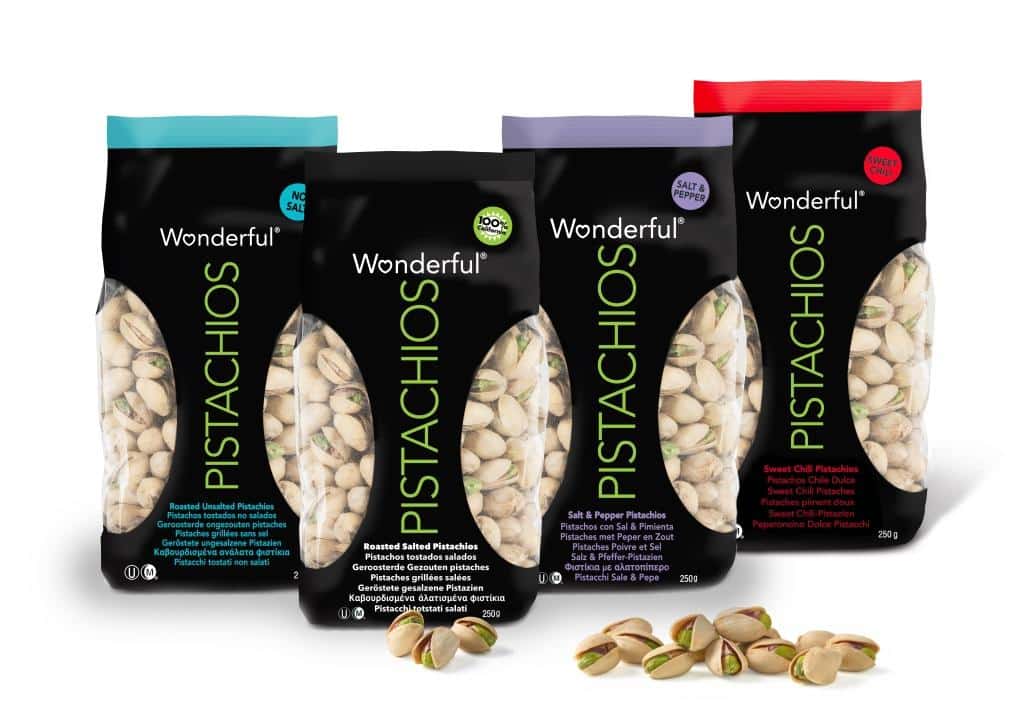 Four colourful bags of Wonderful Pistachios—Roasted Unsalted, Roasted Salted, Salt & Pepper, and Sweet Chilli—stand upright. Each bag has a black centre with clear side panels showing pistachios inside. A few shelled pistachios lie in front.
