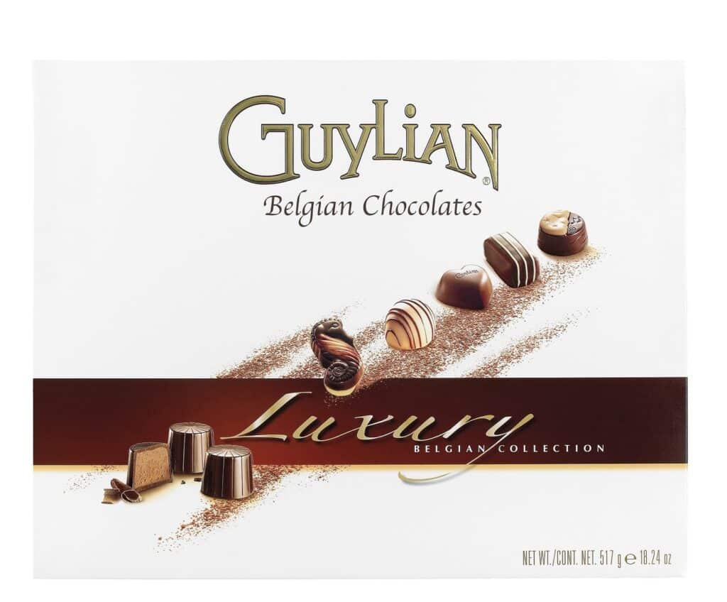 A box of Guylian Belgian Chocolates with a white background. The lid shows various chocolates with swirls, stripes, and marbled patterns. The words "Luxury Belgian Collection" appear in gold and white text across a brown ribbon.