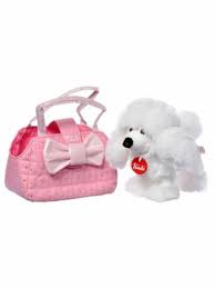 A small white plush poodle toy with a red tag on its collar sits next to a quilted pink handbag decorated with a large bow and two handles. The poodle appears soft and fluffy, and the handbag is stylishly designed for children.