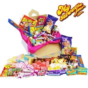 A box overflowing with assorted colourful retro sweets, including lollies, fizzy sweets, Love Hearts, Refresher bars, and sherbet sticks. The logo “My Sweetie Jar” appears in the top right corner. Bright pink tissue paper lines the box.