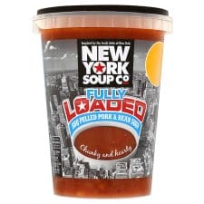 A plastic tub of New York Soup Co. Fully Loaded BBQ Pulled Pork & Bean Soup. The label is black and white with a city skyline background, bold white and red text, and an image of a sunset. The soup inside is reddish-brown and chunky.