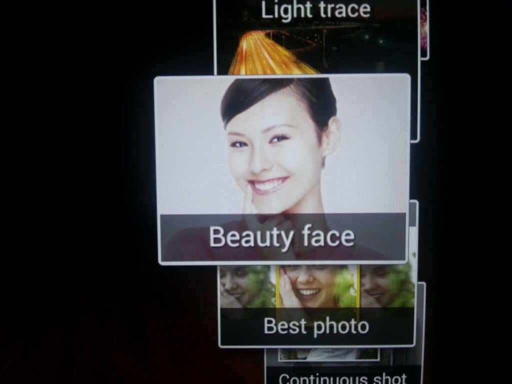 A camera screen displays mode options. The highlighted option shows a smiling woman with dark hair and the text “Beauty face.” Other visible options below include “Best photo” and “Continuous shot.” The background is mostly black.