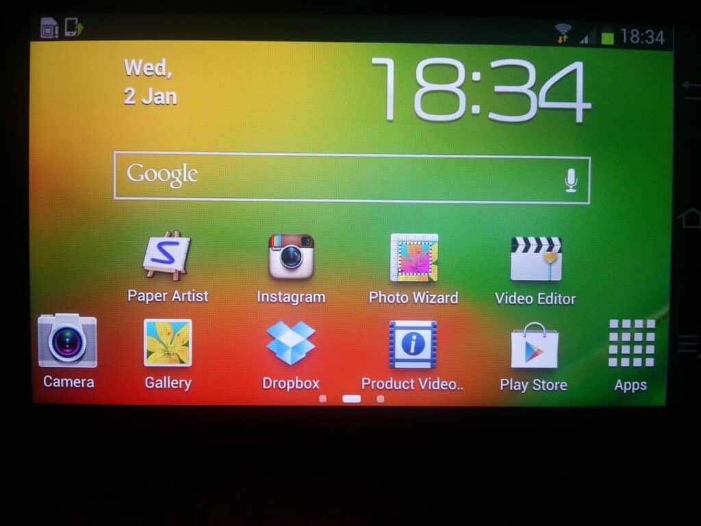 A smartphone home screen displays the date and time (Wed, 2 Jan, 18:34) at the top. Below is a Google search bar, and underneath are app icons: Camera, Gallery, Paper Artist, Instagram, Dropbox, Product Video, Photo Wizard, Video Editor, Play Store and Apps.