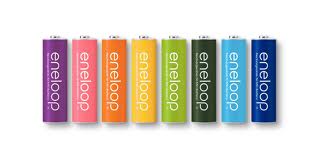 Eight Eneloop rechargeable AA batteries stand upright in a row, each a different colour: purple, pink, orange, yellow, light green, green, black, and blue, all with "eneloop" written vertically in white text on the front.