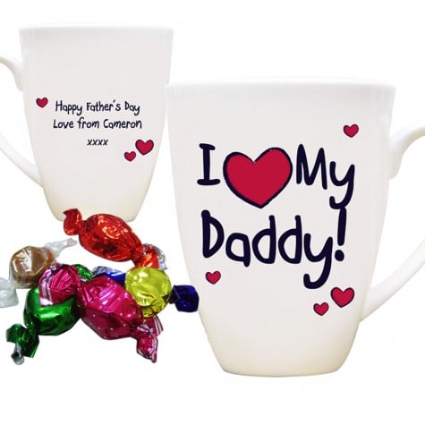 Two white mugs are shown. One reads “I ♥ My Daddy!” with pink hearts. The other says, “Happy Father’s Day Love from Cameron xxxx.” Colourful wrapped sweets in red, green, pink, yellow, silver, purple, and blue are placed beside the mugs.