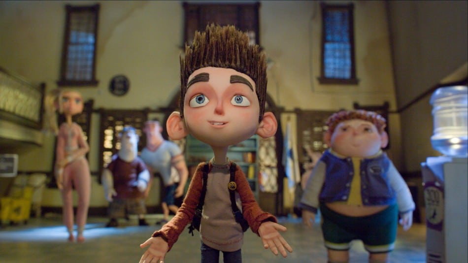 A stop-motion animated boy with spiky brown hair and large blue eyes stands smiling with arms open. Behind him, four other animated characters—two boys, a girl, and a man—stand in a dimly lit room with barred windows and scattered light.