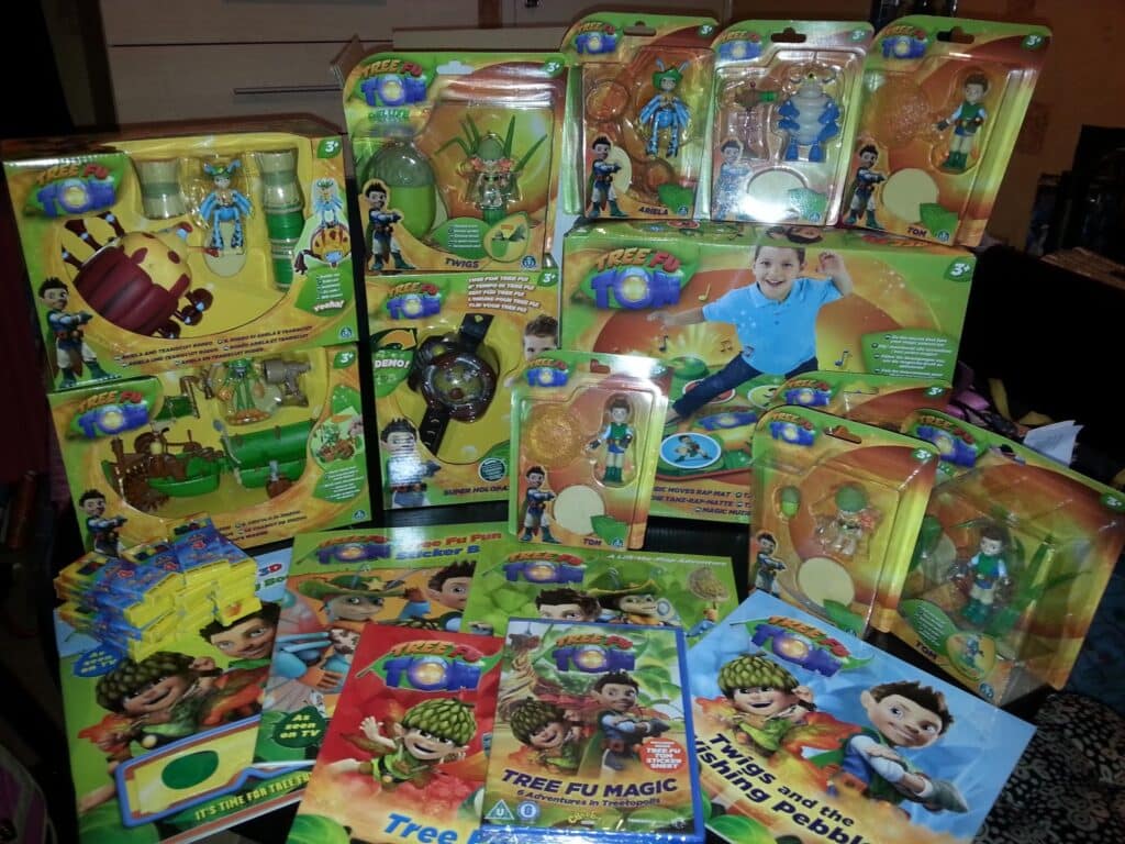 A colourful assortment of Tree Fu Tom toys and books, including action figures, playsets, watches, and storybooks, all featuring characters from the children’s TV show. The items are arranged on a flat surface with bright yellow and green packaging.