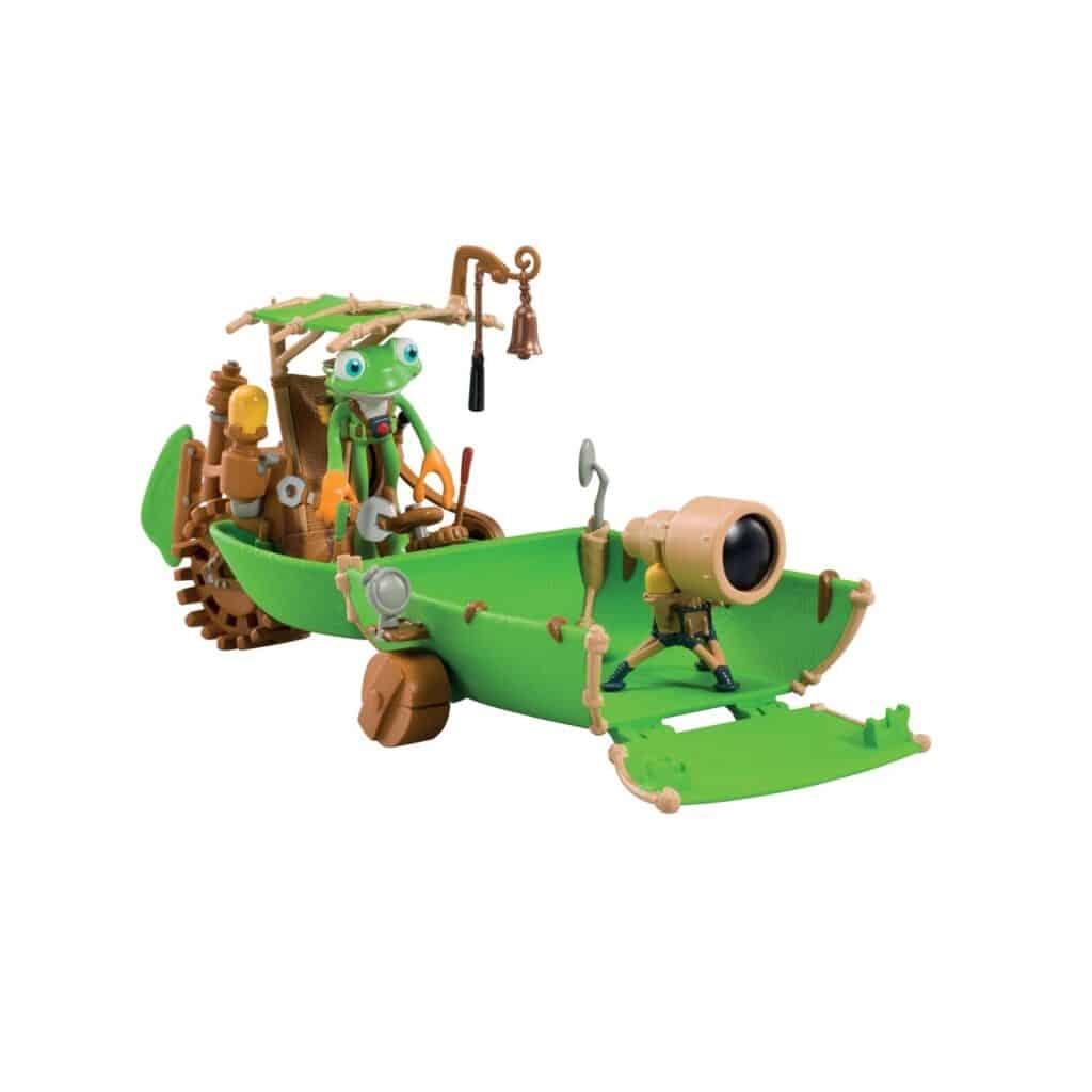 A green, toy vehicle resembling a boat with wheels features cartoonish frog and insect characters. The front has a large lens-like device, and the frog stands at the back under a leafy canopy, holding the controls. The vehicle is detailed with brown and tan parts.