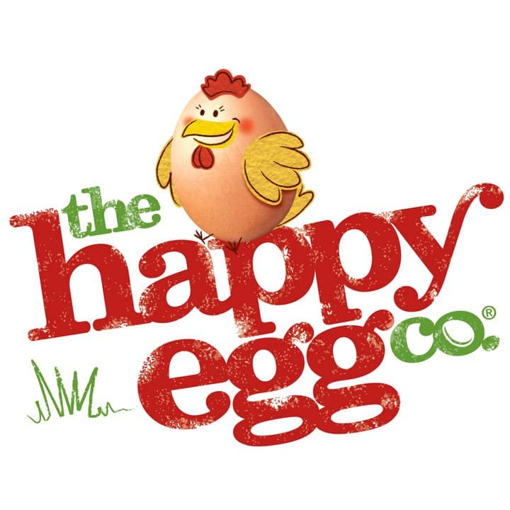 A cartoon chicken stands above bold, red text reading "happy egg" with green text "the" and "co." A tuft of green grass appears near "the." The chicken looks cheerful, with wings spread and a red comb. The design has a playful, hand-drawn style.