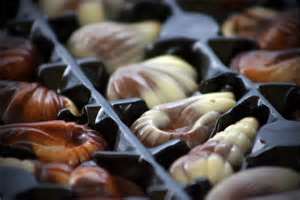 A close-up of assorted seashell-shaped chocolates in a plastic tray, featuring swirls of milk and white chocolate. The chocolates are glossy and detailed, each resting in its own compartment, ready to be enjoyed.
