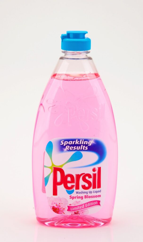 A bottle of Persil washing-up liquid with pink liquid inside. The label reads "Sparkling Results," "Persil," "Spring Blossom," and "Limited Edition." The bottle has a blue flip-top cap and is photographed against a white background.