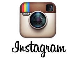 Square vintage-style camera icon with a large lens in the centre, rainbow stripes in the top left corner, and a brown top border. Below the icon, the word "Instagram" is written in a cursive black font.