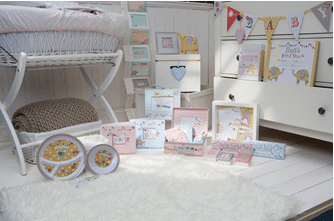 A cosy, white nursery with a wicker bassinet, a fluffy rug, and a chest of drawers. Pastel baby gifts, keepsake boxes, plates, and decor with elephant designs are arranged on the floor. Colourful bunting and cards hang on the chest of drawers and wall.