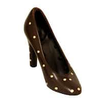 A high-heeled shoe made of dark chocolate, decorated with evenly spaced small white chocolate dots, sits against a plain white background. The shoe is realistic in shape and detail, resembling a classic court shoe.