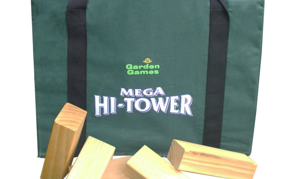 A green carrying bag labelled “Garden Games Mega Hi-Tower” sits upright. In front of it are five large, rectangular wooden blocks, some stacked and some lying flat, hinting at a giant outdoor Jenga-style game. The Garden Games logo is in the bottom right corner.