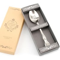 A silver spoon with ornate handle is placed in a grey presentation box labelled “STERLING SILVER.” The spoon is engraved on its bowl. The box is next to a beige lid decorated with elegant white designs and the words “STERLING SILVER” and “MADE IN ENGLAND.”.