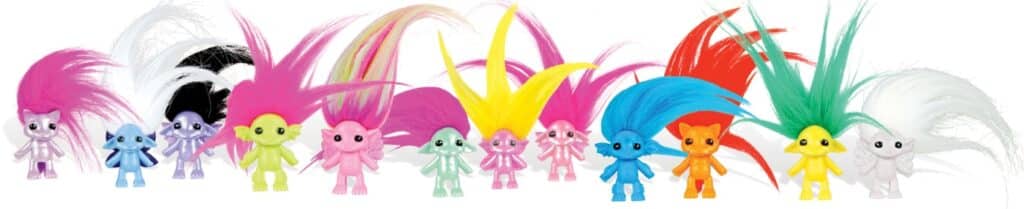 A row of colourful troll dolls with large, wild hair in various bright colours, including pink, yellow, blue, green, red, white, and black. Each doll has a different body colour and wide eyes, standing side by side against a white background.