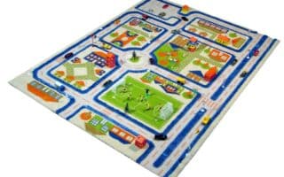 Children’s play rug showing a small town with winding blue roads, houses, buildings, cars, trees, a football pitch with players, and playgrounds. The rug has colourful residential and urban areas arranged in a neat, playful pattern.