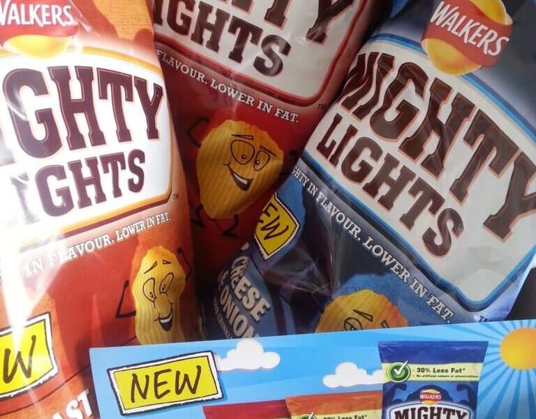 Three bags of Walkers Mighty Lights crisps—Roast Chicken, Cheese & Onion, and another flavour—are propped up behind a cardboard display showing all three flavours and advertising “30% less fat.” Cartoon crisp characters and bold “NEW” signs are visible.