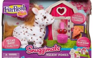 A FurReal Friends Snuggimals Walkin’ Ponies toy set is shown. The box features a white plush pony with brown spots, a pink barn with a heart-shaped window, toy carrots, and accessories. The packaging is colourful with playful graphics and product details.