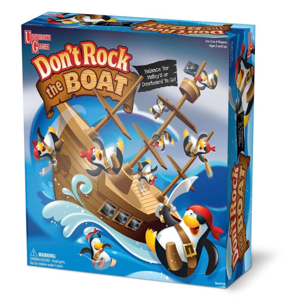 A game box for "Don't Rock the Boat" features cartoon pirate penguins balancing on a wooden ship rocking on ocean waves. The penguins wear pirate hats, bandanas, and eye patches. The tagline reads, “Balance Yer Mateys or Overboard Ye Go!”.
