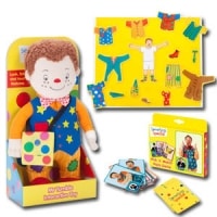 A boxed soft doll with red hair, colourful clothes, and button accessories sits next to a yellow magnetic dress-up board with clothing pieces and a child illustration, plus a matching card game set in yellow packaging.