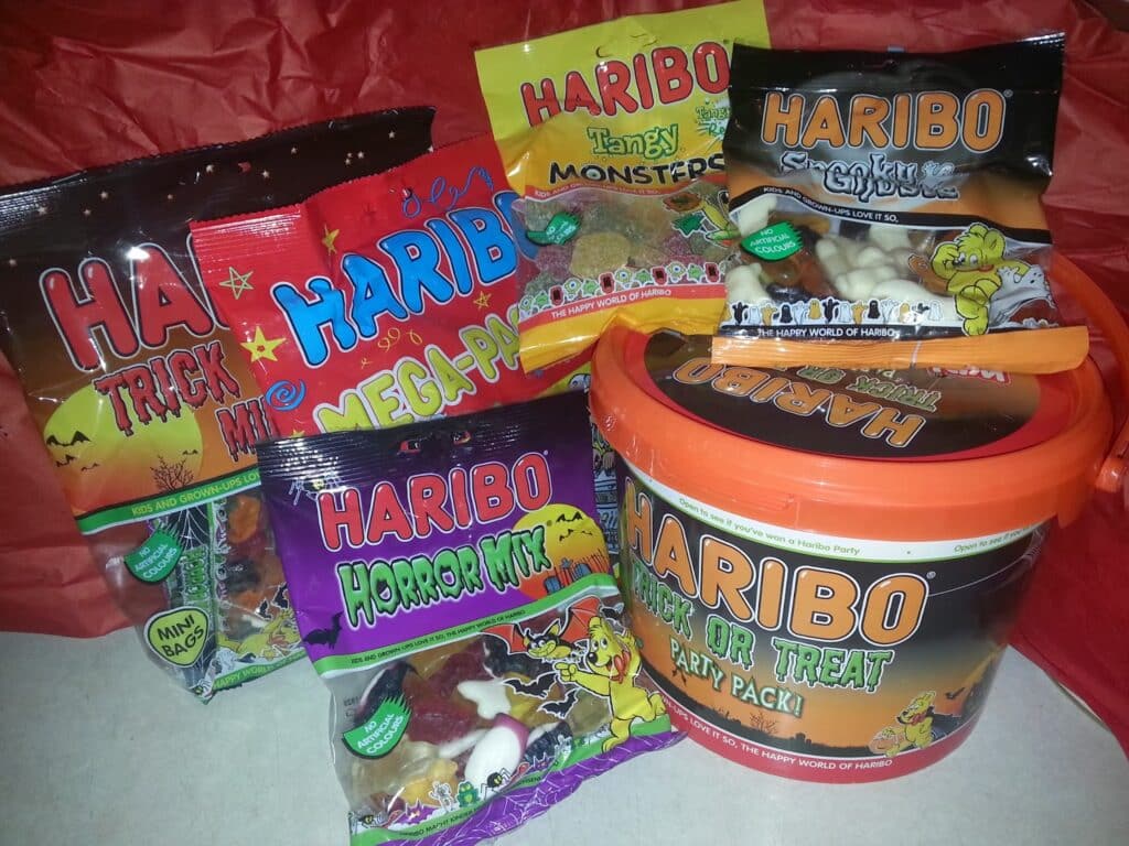 Several Halloween-themed Haribo gummy sweet packs are displayed, including bags labelled Trick or Treat, Horror Mix, Mega-Pack, Tangy Monsters, and Crokriz, along with a large orange tub labelled Trick or Treat Party Pack, all featuring festive Halloween graphics.