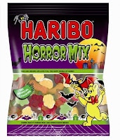 A Haribo Horror Mix sweet bag features a Halloween theme with a yellow bear, bats, a spooky house, and a full moon on the packaging. The bag contains various jelly sweets shaped like bats, pumpkins, and other spooky shapes.
