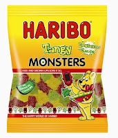 A yellow and red bag of HARIBO Tangy Monsters gummy sweets features the HARIBO bear mascot holding a magnifying glass. The bag has images of monster-shaped sweets and green text reading "Tangy Monsters" with a "Sour Sugar Blast" label.